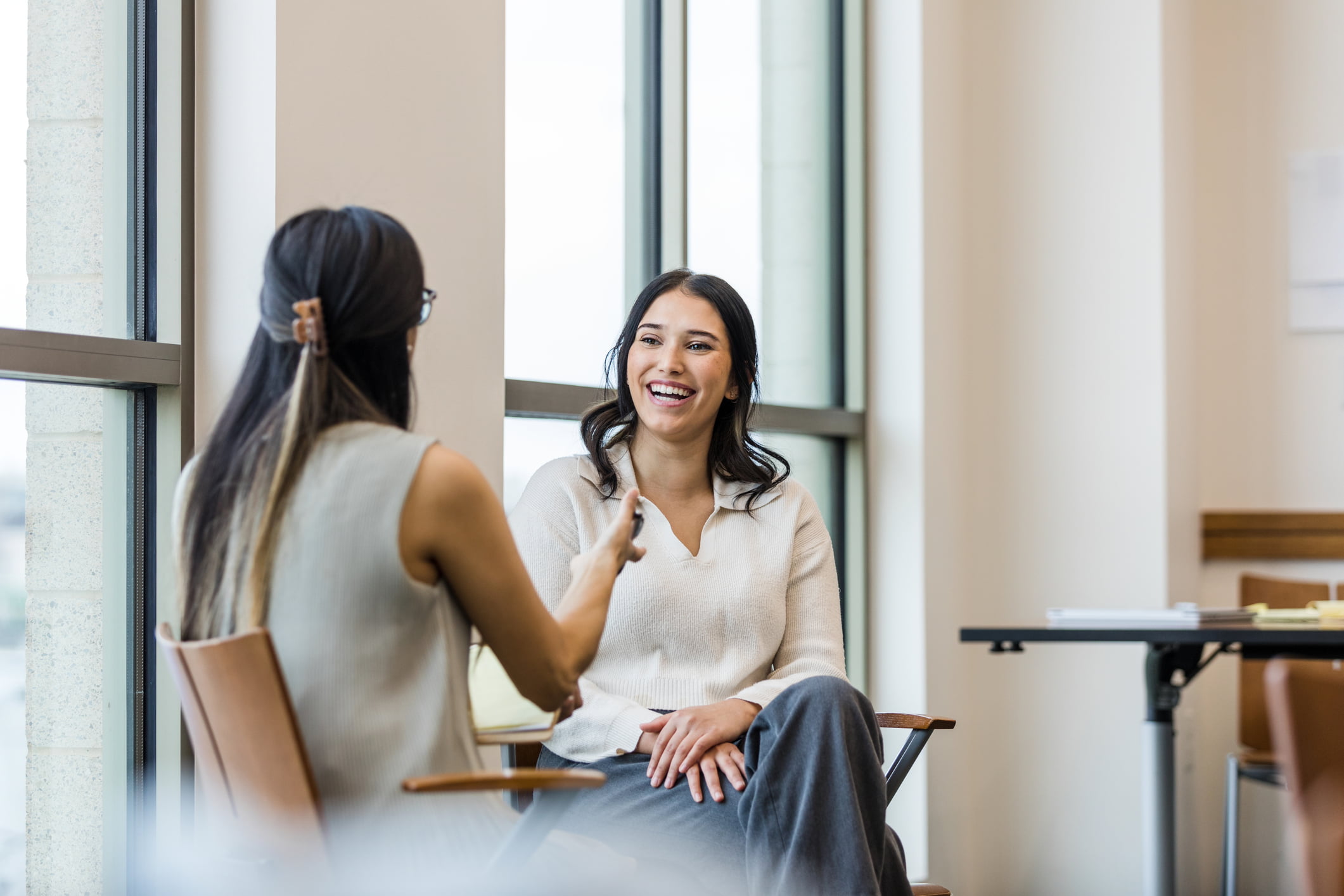 Young adult female patient smiles as unrecognizable female counsellor speaks