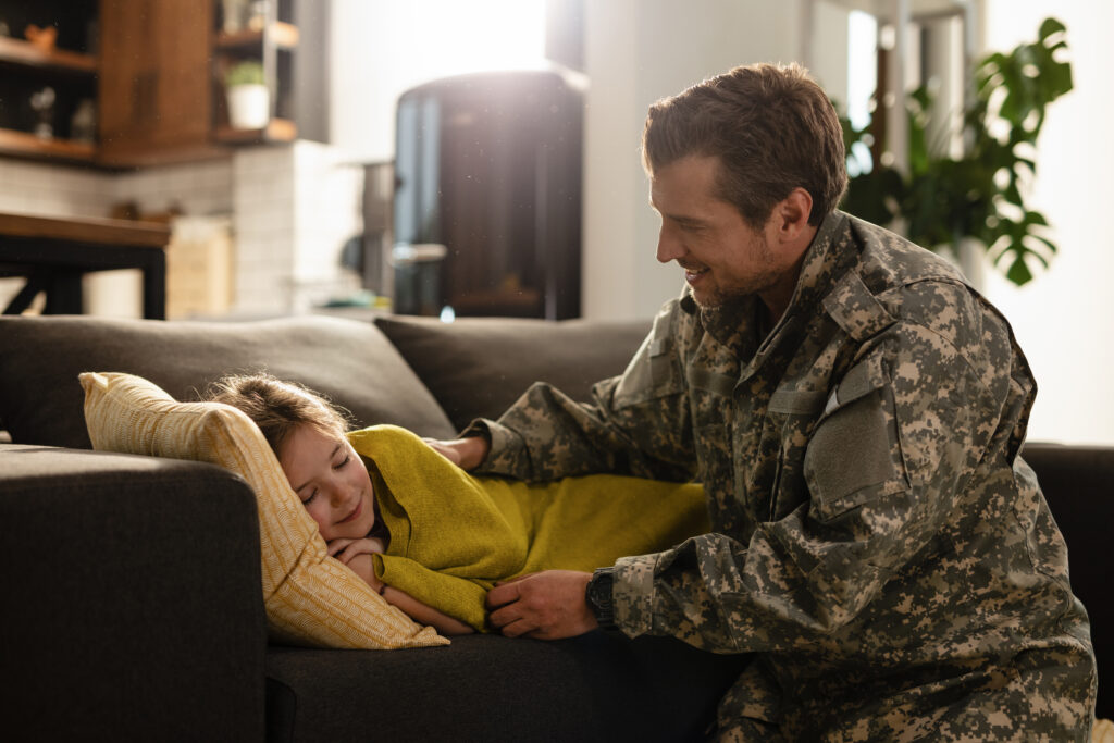 Small girl sleeping carelessly on the sofa while veteran dad is next to her.